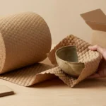 Kraft bubble paper roll wrapping ceramic product on packing workbench — plastic-free paper cushioning for eco-friendly export packaging