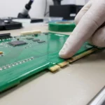 Technician applying green PET masking tape to a PCB edge connector