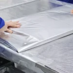 Operator smoothing a large aluminum foil bag on the sealing table